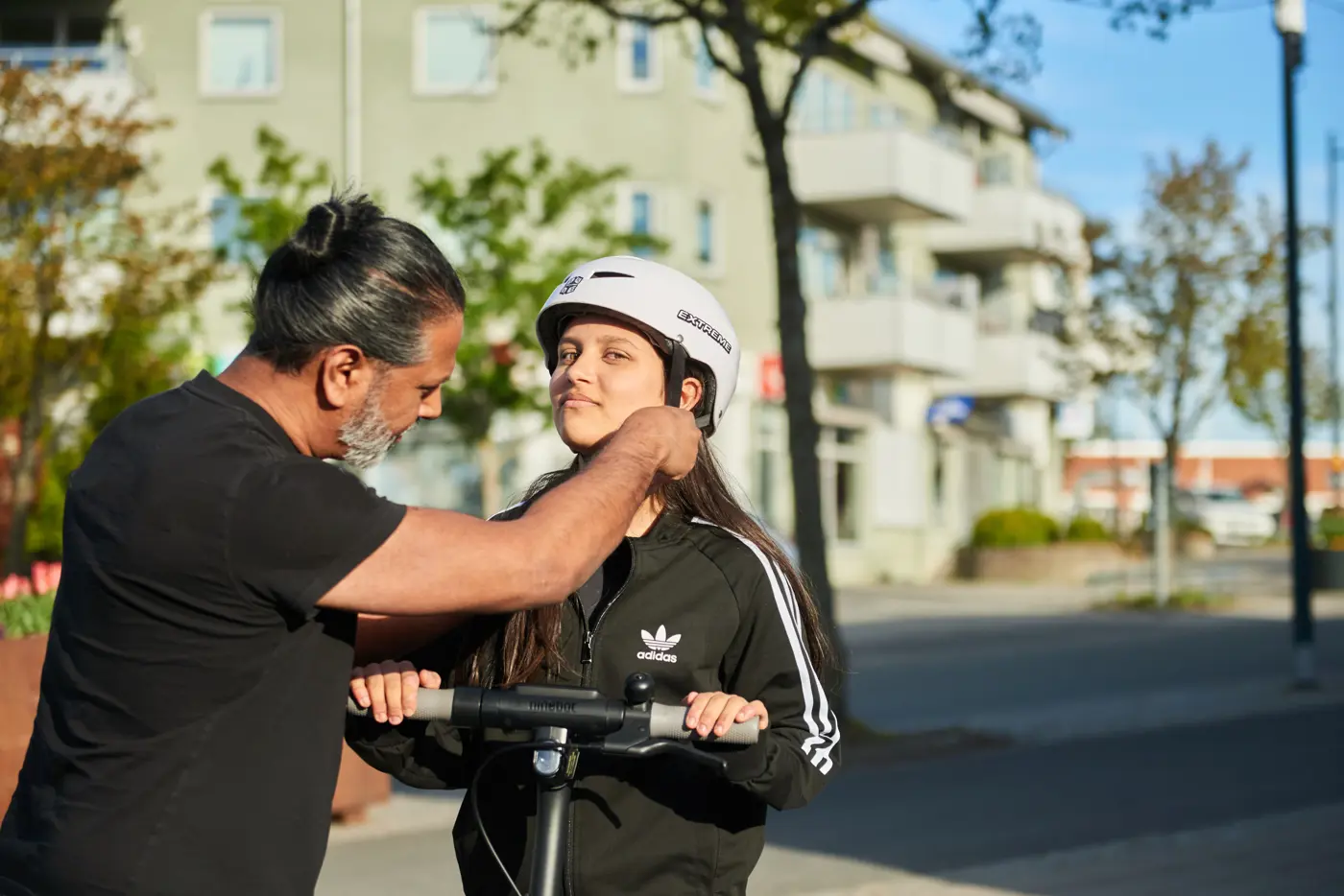 En pappa hjälper din dotter som ska köra elsparkcykel knäppa sin cykelhjälm.