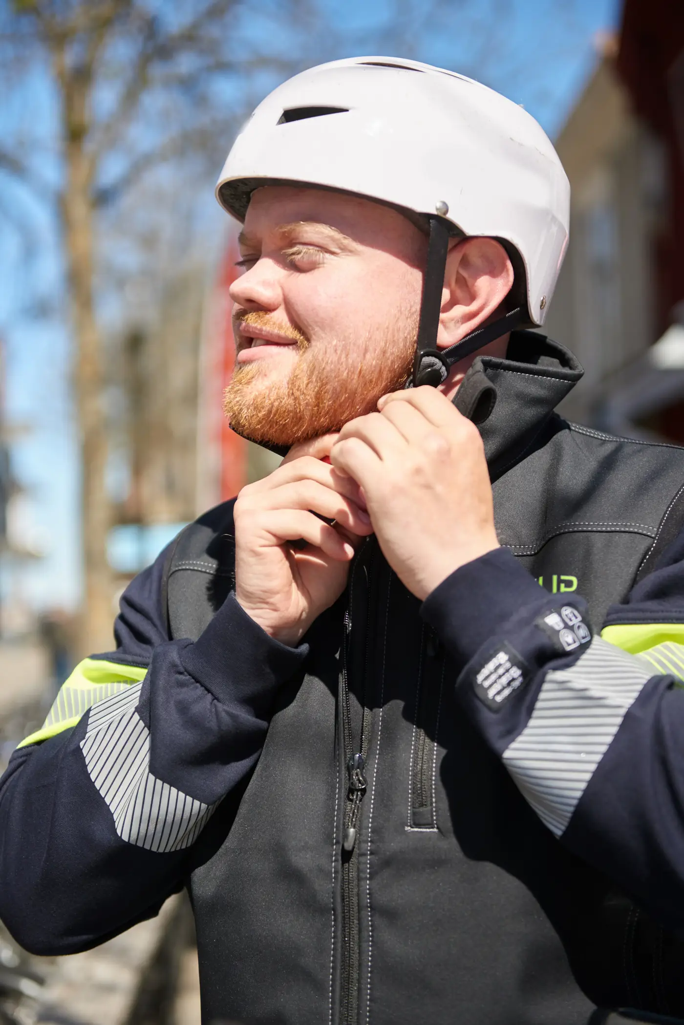 En man med arbetskläder knäpper på sig en cykelhjälm.